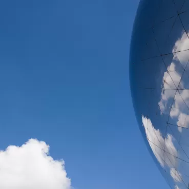 Eine moderne, glänzende Gebäudefassade spiegelt den blauen Himmel mit weißen Wolken