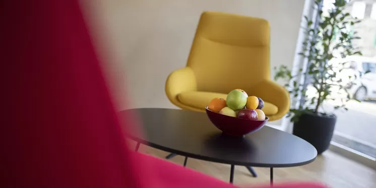 Moderne Lounge-Ecke mit einem gelben Sessel, schwarzem Tisch und einer Schale mit frischem Obst vor einer Fensterfront